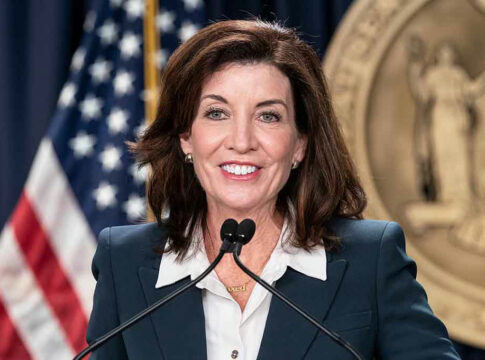 Woman speaking at podium with American flag behind.