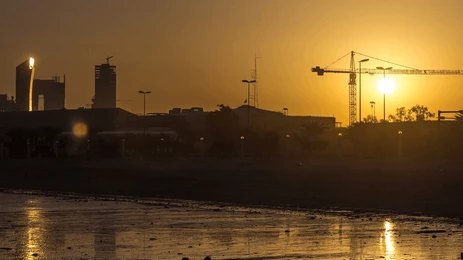City skyline with construction cranes at sunset by a reflective shoreline