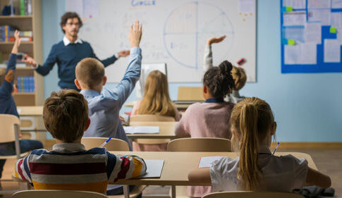 Students raising hands in a classroom as a teacher leads a lesson