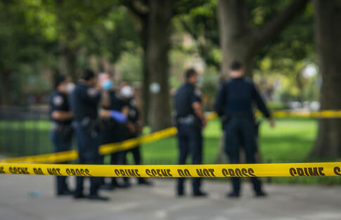 Police officers behind yellow crime scene tape in park.