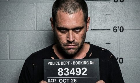 A man posing for a police mugshot with a booking sign